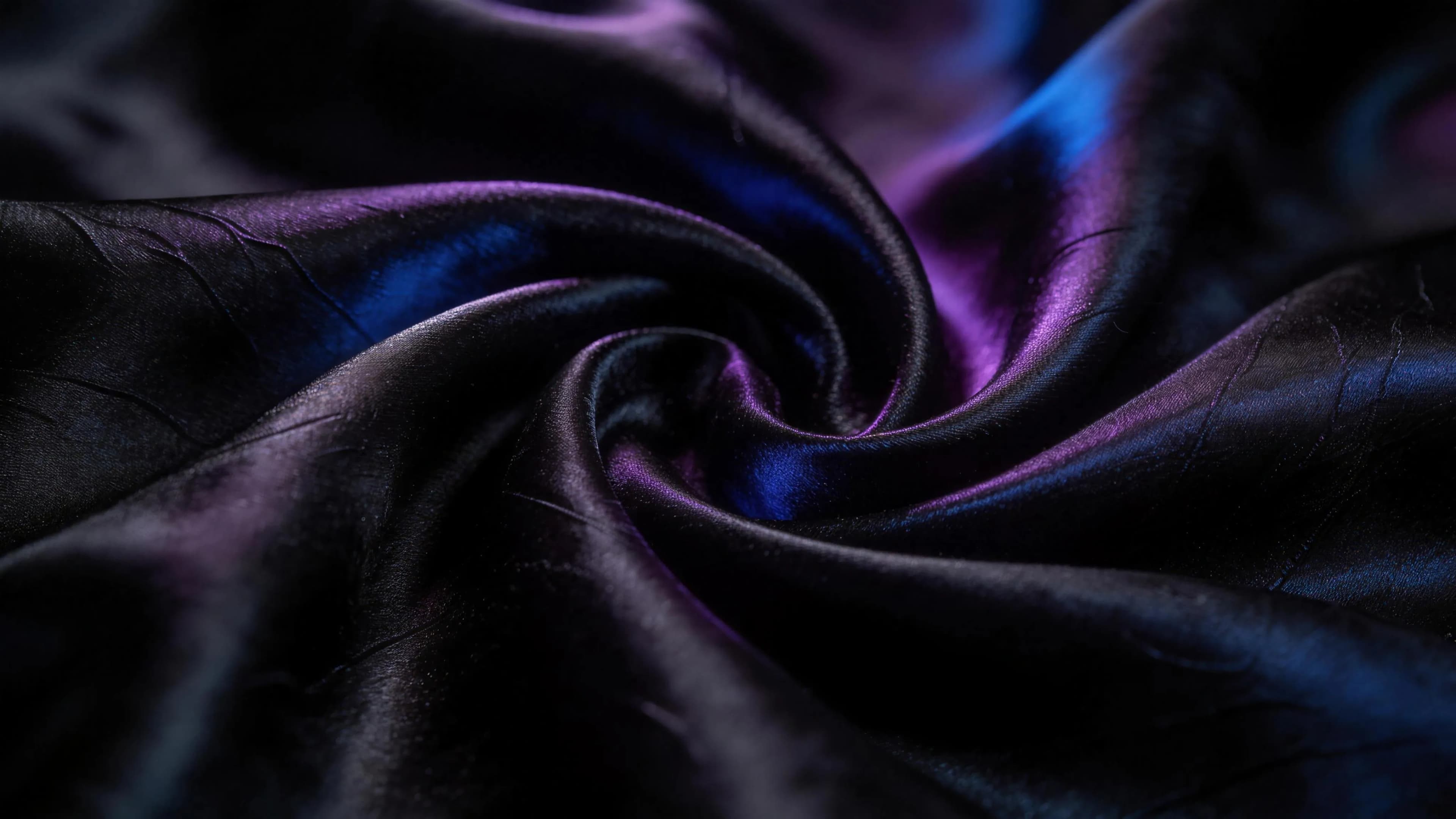 Black silk folding into a swirl, catching violet and blue light in the dark.